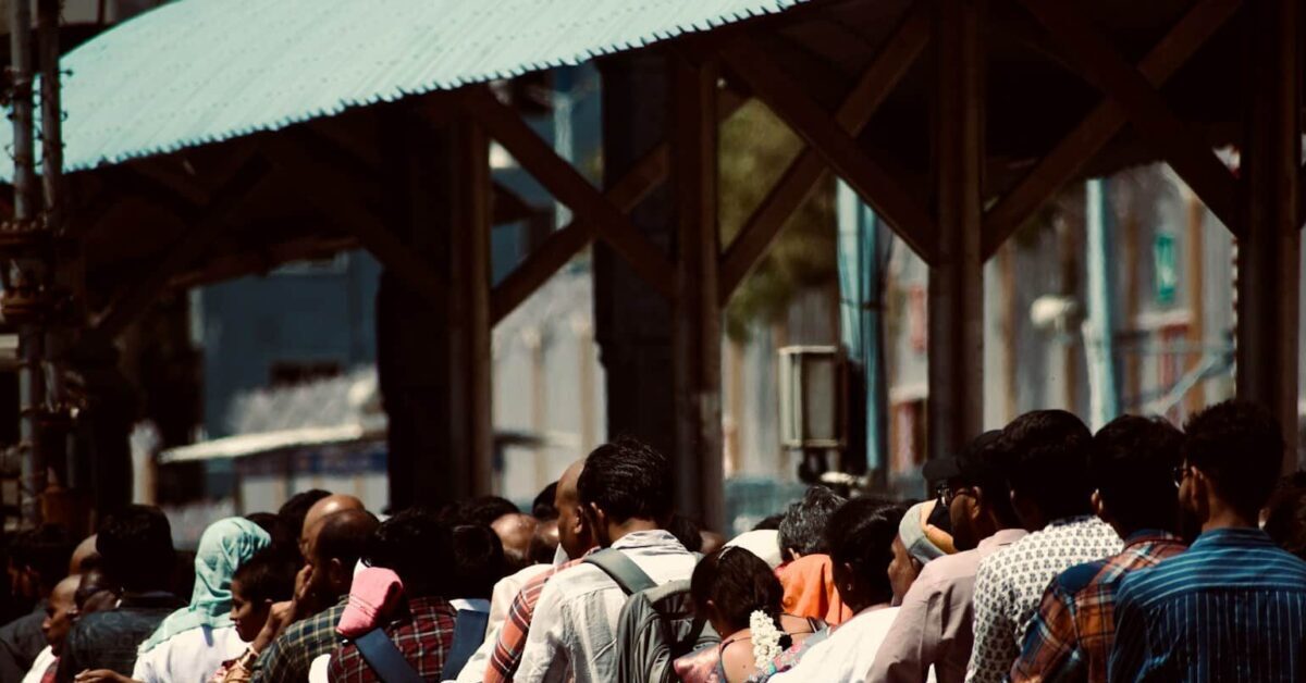 Caste-Based A large crowd waiting behind a metal barrier.